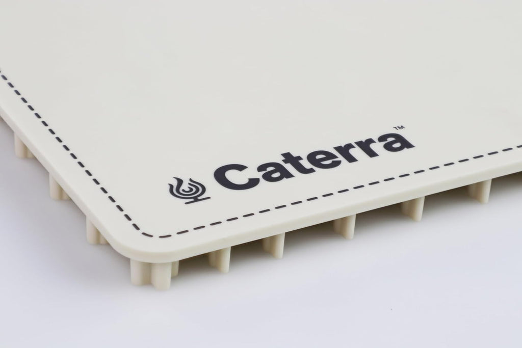 Corner detail of the cream warming mat showing the Caterra logo, dashed border print and silicone feet